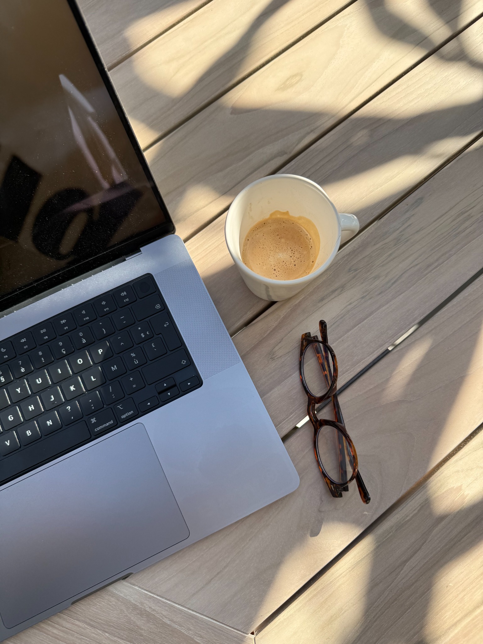 Notebook, café e óculos sobre uma mesa iluminada pelo sol